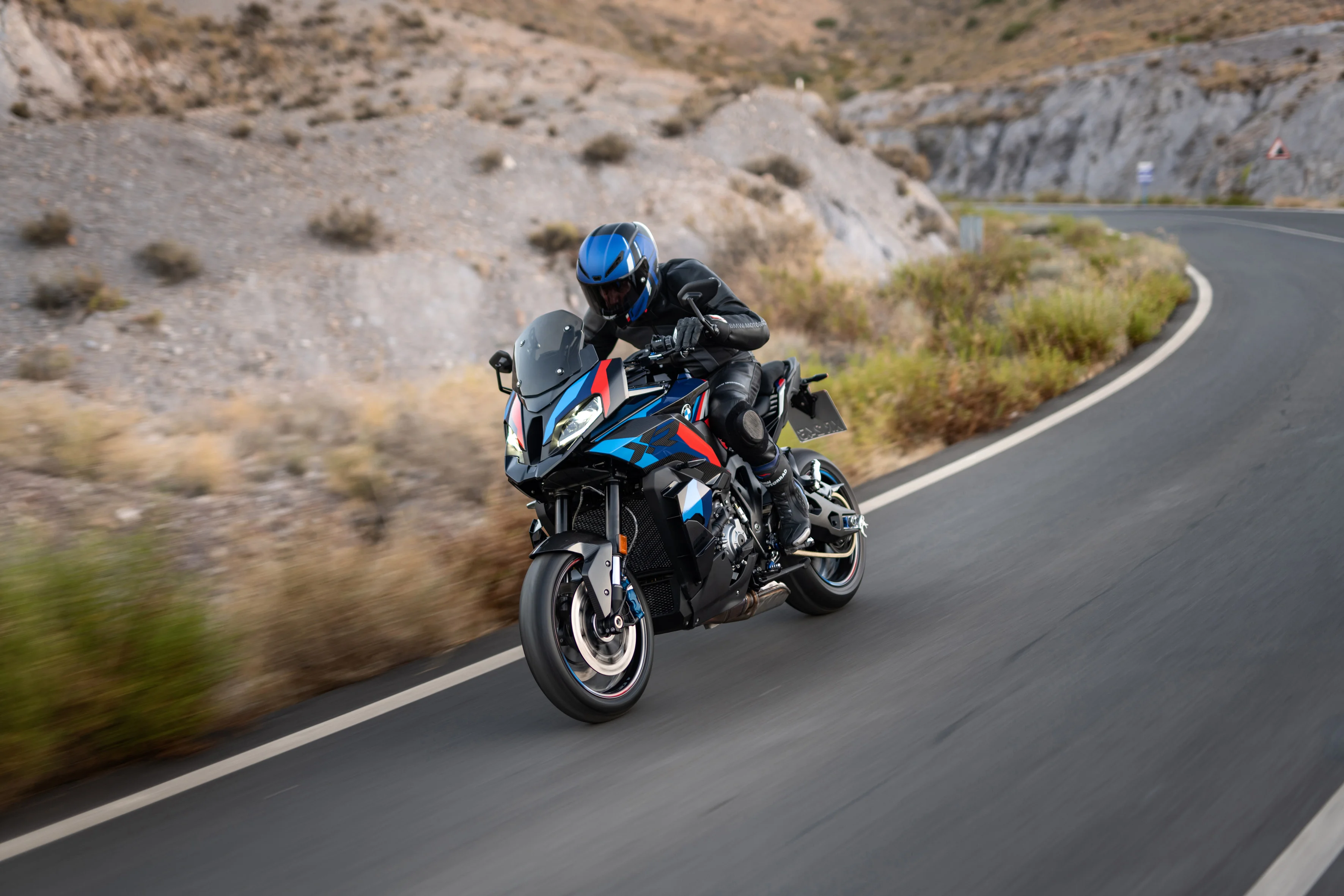 2026 BMW M 1000 XR performance crossover riding on a mountain road with rocky terrain